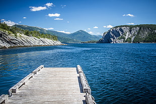gray wooden dock on body of water near mountains under blue and white sunny sky during daytime, norris point