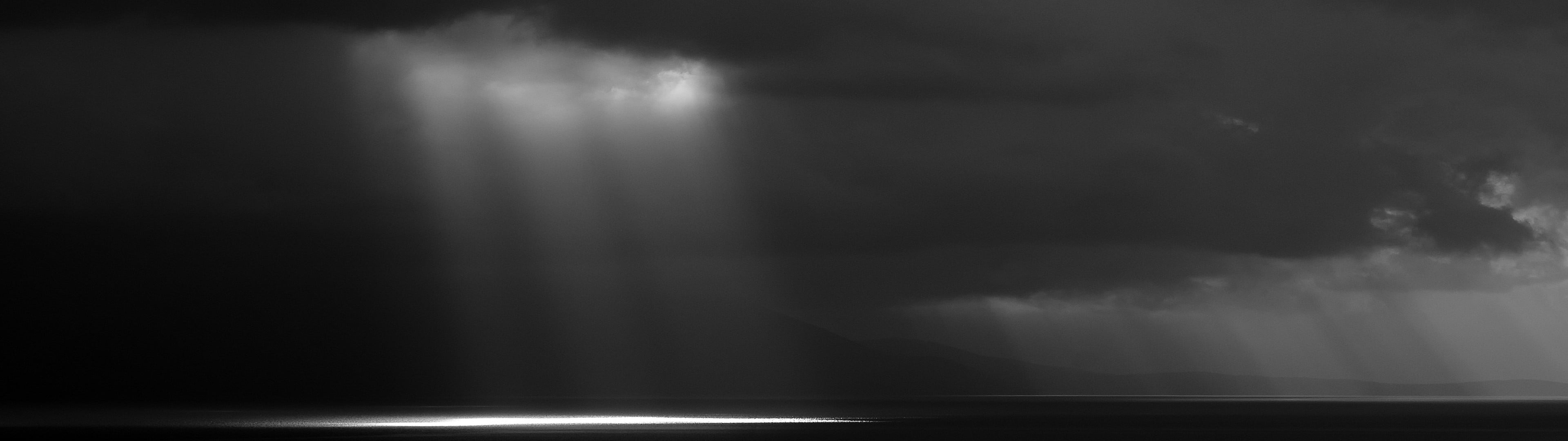 grayscale photo of sunlight peeking from body of clouds