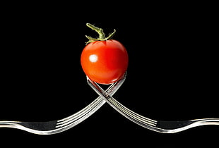 red tomato on two stainless steel forks with black background