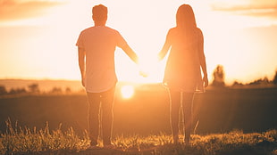 couple holding hands standing towards golden hour