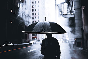 photo of person using umbrella passing high rise buildings