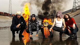 group of four men in assorted clothes with fire on background