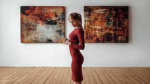 woman in red long-sleeved dress standing between two abstract paintings