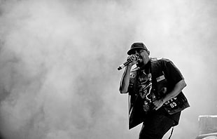 grayscale photography of a man wearing vest and t-shirt on stage singing