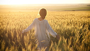 woman in white long-sleeved dress walking through wheat field