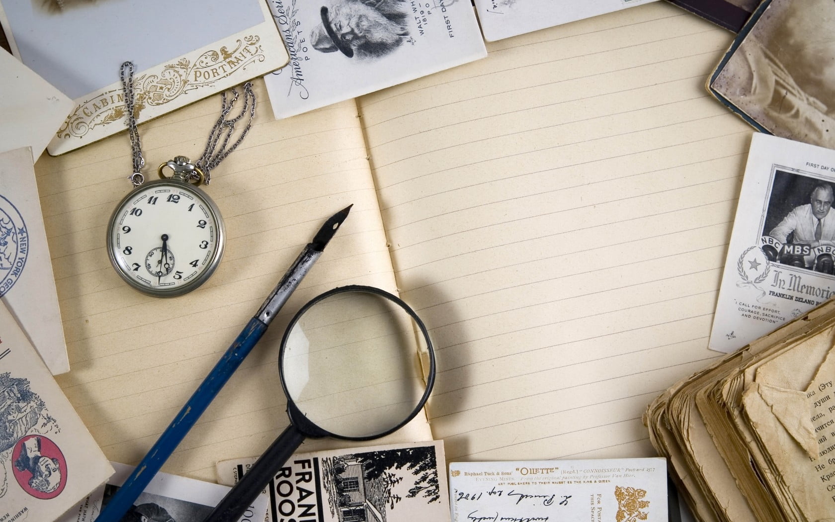 photo of blue paint brush, black magnifying glass, and assorted papers on brown notebook page