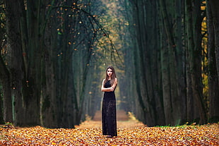 woman with black floral sleeveless standing on brown leaves covered pathway