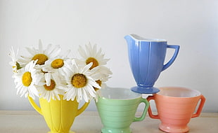 four assorted colors of pitchers and daisy flowers on top of beige surface