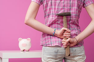 photo of person holding brown hammer near piggy bank
