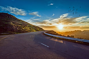 gray concrete road near brown rock cliff with sunset as a background HD wallpaper