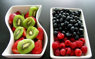 bowl of Kiwi fruit with strawberries next to bowl of blueberries and raspberries