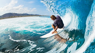 man on surfboard riding wave under blue and white sky during daytime