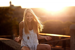 blonde haired woman in white floral lace tank top sitting on concrete surface