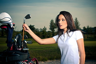 photo of woman wearing white polo shirt while holding brown and gray golf club