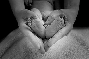 grayscale photo of person holding feet of baby
