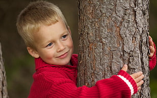 boy in red sweater hugging tree