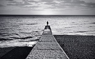 grayscale photo of person standing on sea dock