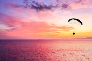 photography of man in parachute above sea under orange sky
