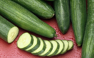 green cucumbers and sliced cucumbers on red surface-top