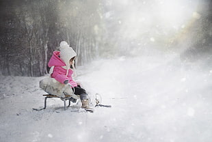 kid in pink bubble hoodie sitting on sled during winter