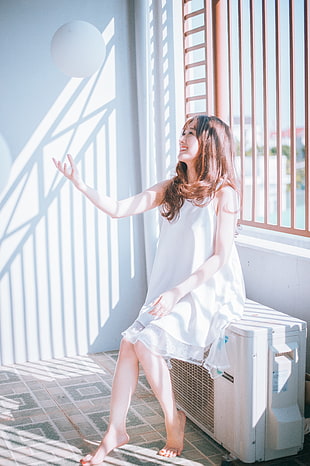 woman wearing white spaghetti strap dress sitting on white air inverter during daytime