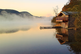 cabin house at lakeside with fog and mountain hills during sunset