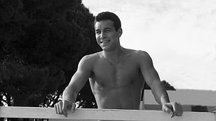 vintage photo of a shirtless man standing behind a white wooden barrier