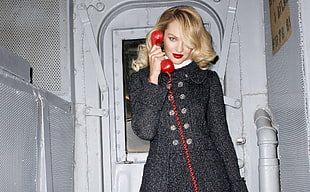 woman wearing black double-breasted coat while holding red telephone