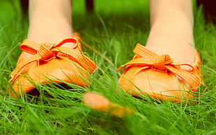 woman wearing pair of orange shoes top of green grass