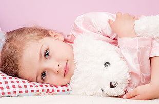 girl wearing pink long-sleeve shirt hugging white dog plush toy