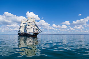 brown sailing ship on body of water under cloudy blue sky