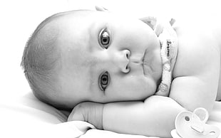 baby lying face down beside pacifier grayscale photography