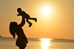 silhouette carrying child during sunset