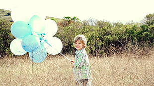 boy in green flannel shirt holding balloons
