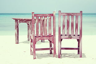 selective focus photography of two brown wooden chairs with table near body of water