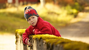 boy wearing Spider-man beanie and red jacket leaning on a mossy bricked wall