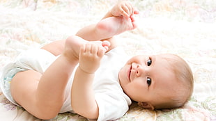 baby lying on bed while holding his feet HD wallpaper