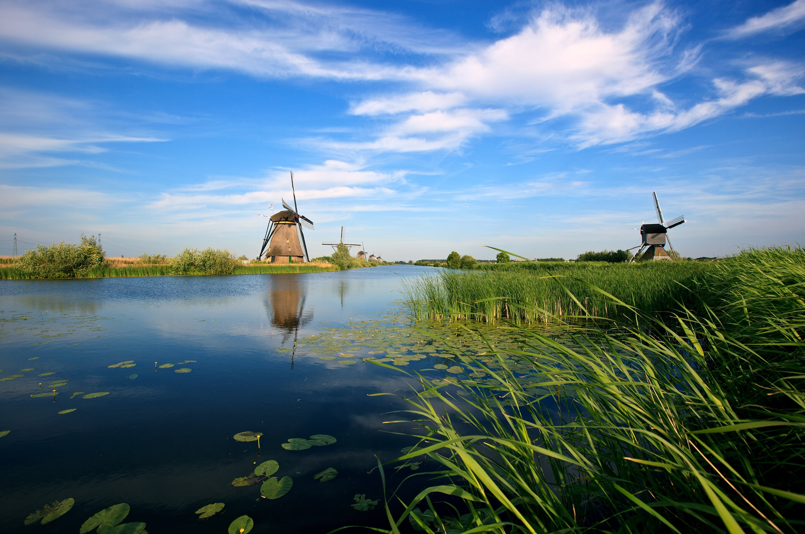 brown watermill surrounded with lake and green grass under blue and white cloudy sky