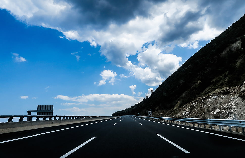 black concrete road between road rails under blue and white clouds during day time HD wallpaper
