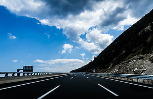 black concrete road between road rails under blue and white clouds during day time