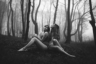 grayscale photo of two women sitting in grass in forest