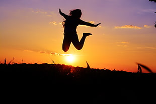 silhouette of girl jumping on grass hill