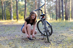 woman in black shirt and blue short shorts sitting beside bicycle