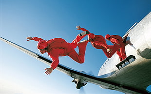 three person jumping off a plane wearing red jumpsuits during daytime HD wallpaper