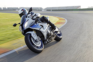 person rides on white and blue sports bike speeding on race track during daytime