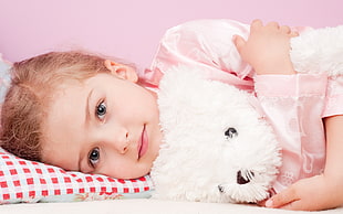girl hugging white bear plush toy while laying down on bed