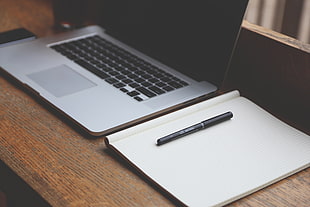 black pen on top of notebook beside MacBook Pro