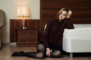 woman wearing brown sweater and black stockings leaning on white bed