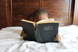 boy reading Holy Bible on white mattress