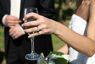 tilt photography of woman in white wedding dress holding champagne flute beside man wearing black suit jacket
